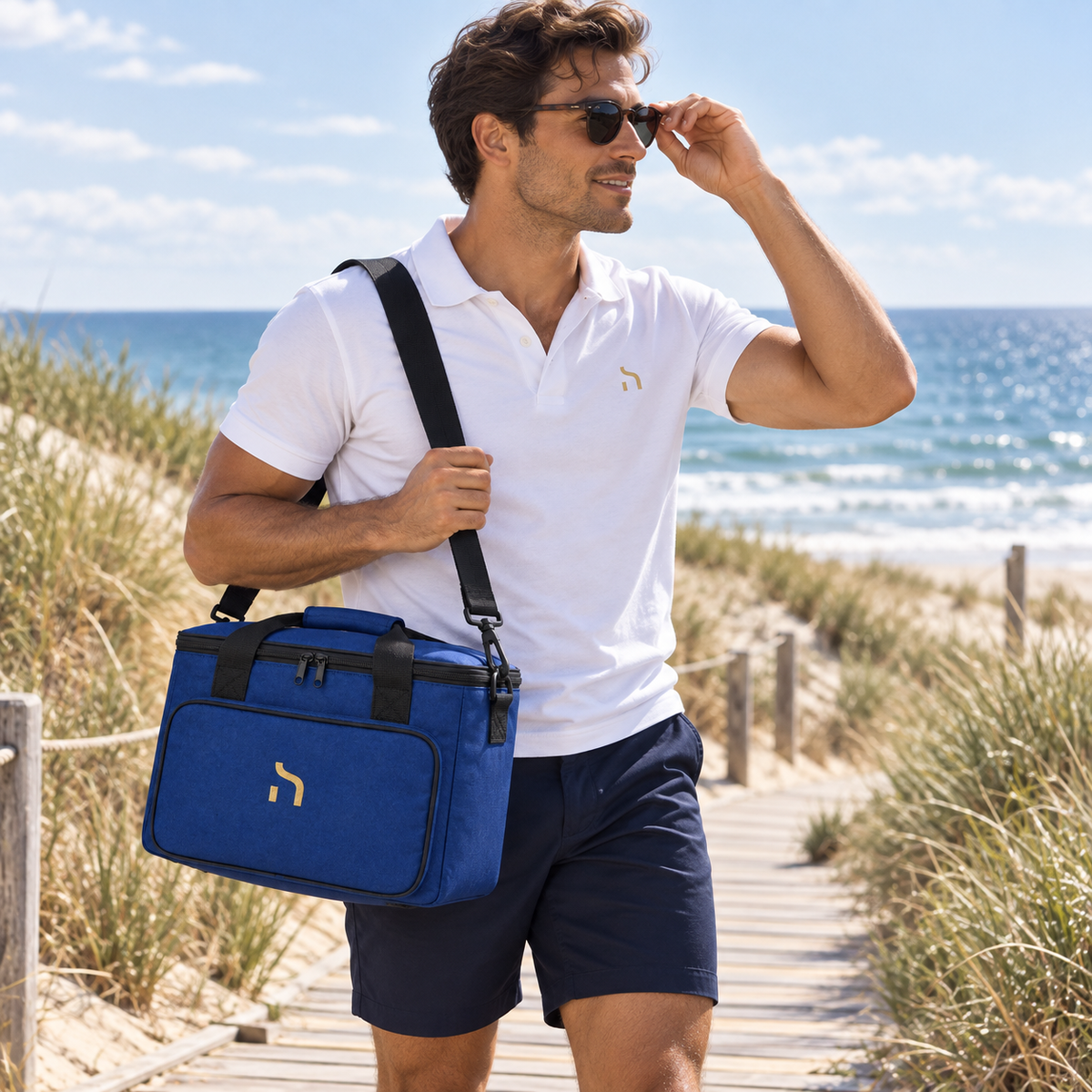 Mann trägt die cobalt-blaue Haensch Coast Kühltasche und ein weißes Haensch Coast Poloshirt auf einem Dünenweg.