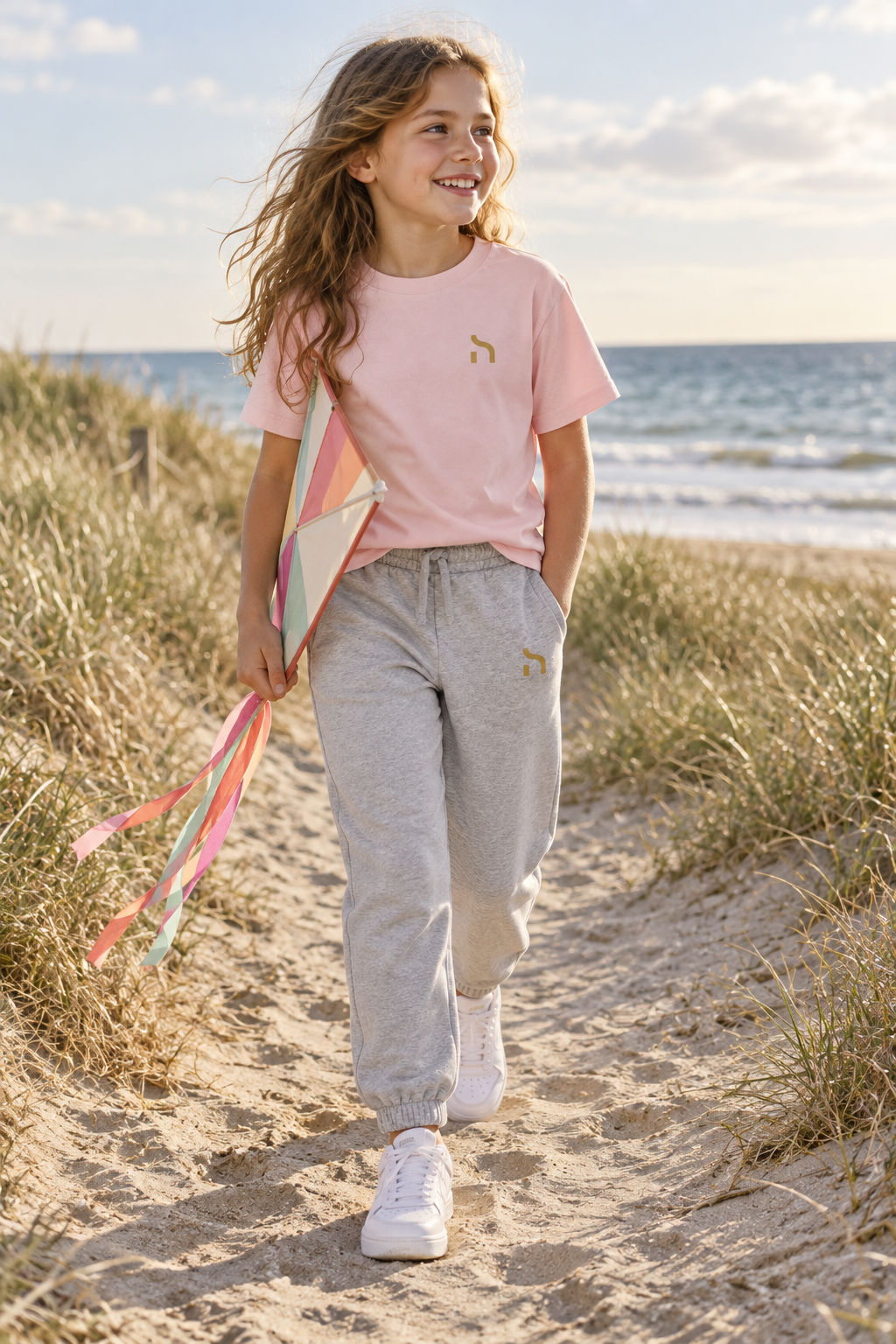 Mädchen trägt die graumelierte Haensch Coast Kids Jogginghose und ein rosafarbenes Haensch T-Shirt auf einem Dünenweg an der Ostsee.