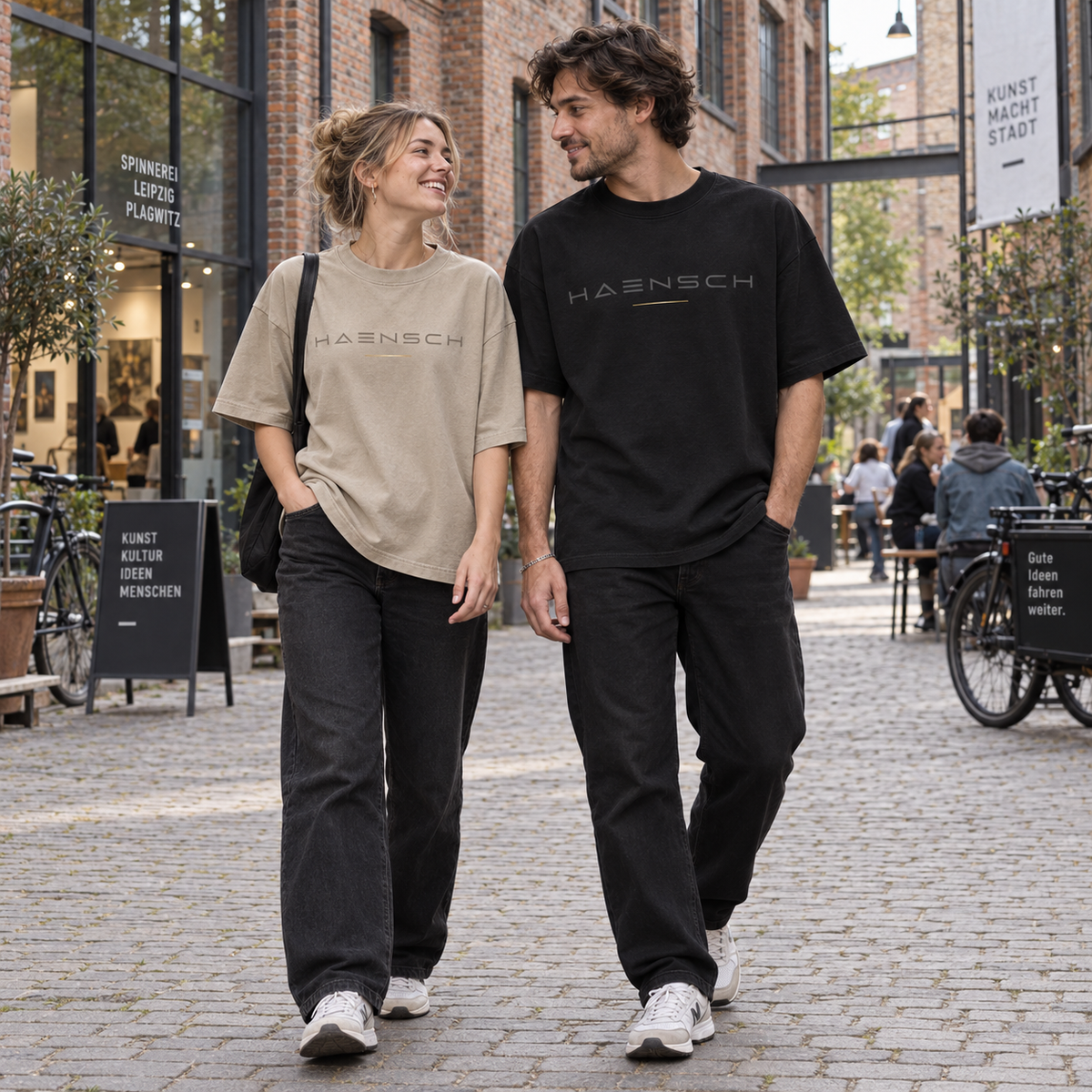 Junges Paar in Leipzig-Plagwitz trägt das Haensch Studio Oversized Box T‑Shirt in Union Beige und Schwarz.