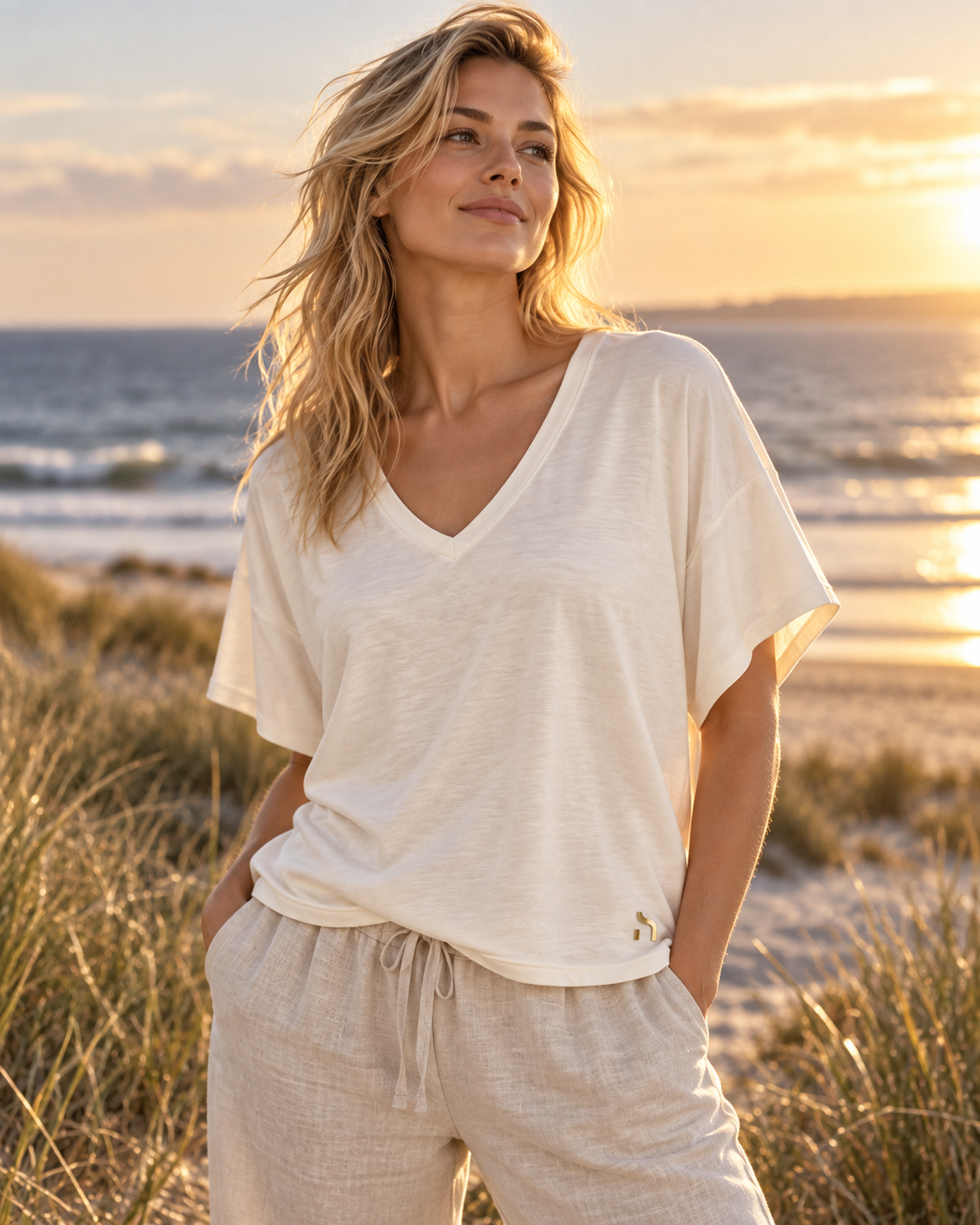 Frau trägt das Haensch Coast Airy Kimono Tee Damen in Coast Ivory mit goldenem H-Logo in einer sommerlichen Dünenlandschaft an der Ostsee