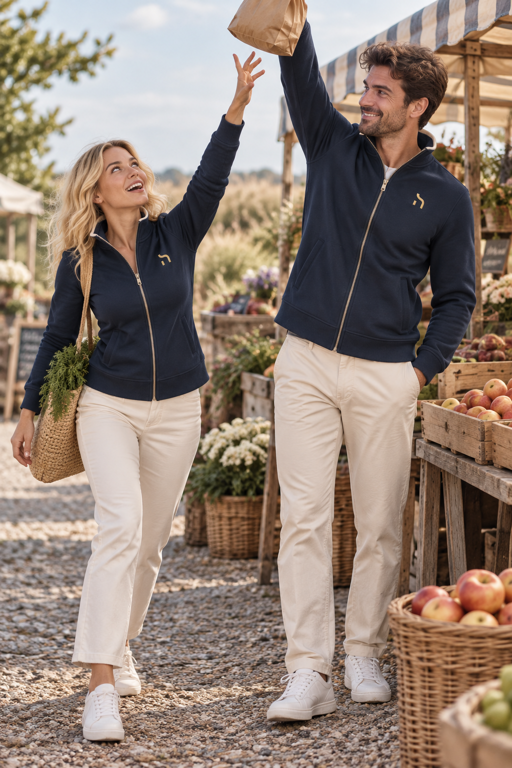 Paar trägt Haensch Coast Premium Sweatjacken in Deep Navy mit goldenen Brustzeichen auf einem offenen Küstenmarkt.