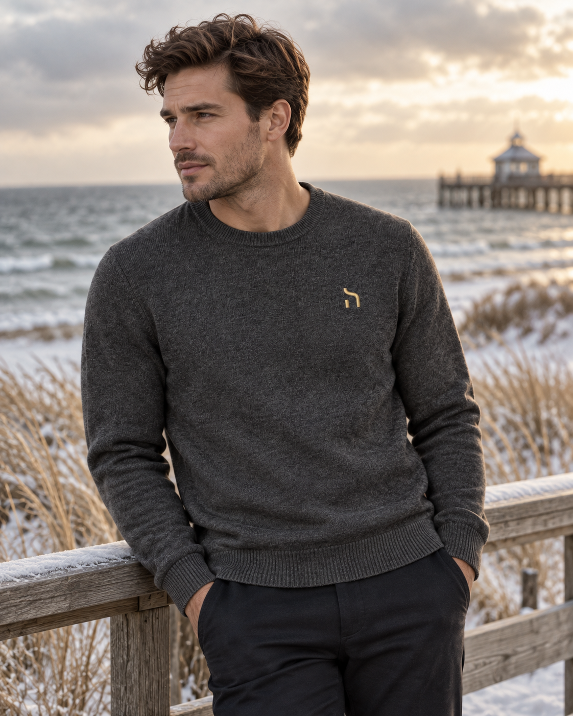 Männliches Model trägt den Haensch Heritage Knit Sweater Herren in Iron Grey mit goldenem Hänsch-H-Signet vor winterlicher Ostsee- und Stegkulisse