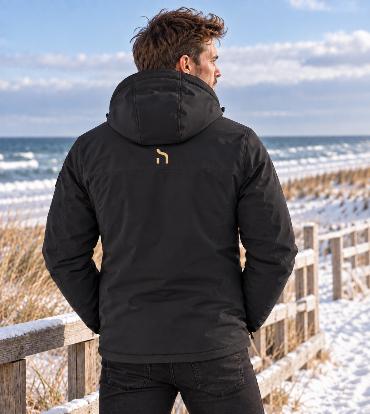 Rückenansicht eines männlichen Models in der Haensch Northern All Weather Winter Jacket Herren in Winter Black an der verschneiten Ostseeküste