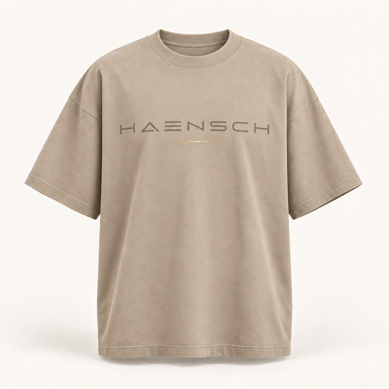 Beigefarbenes Haensch Studio Oversized Box T‑Shirt mit tonalem HAENSCH-Schriftzug und feiner goldener Linie in der Vorderansicht.